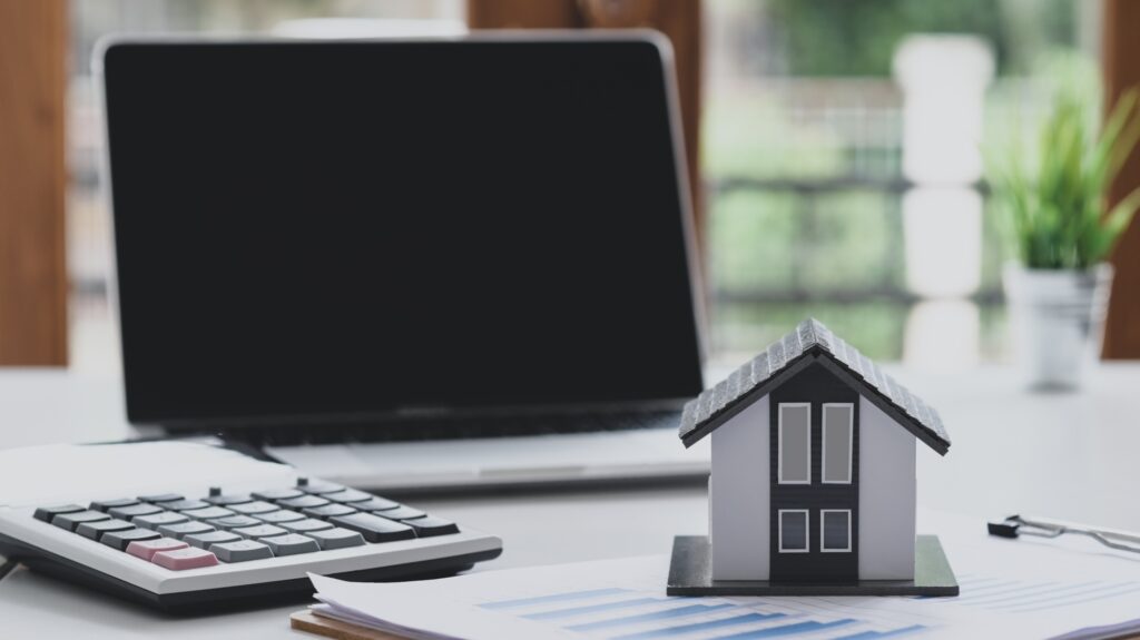 Model house puts a graph document with a calculator and a laptop, Real estate business concept.